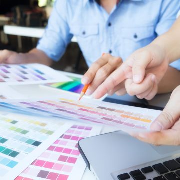 Two people working on a project with a laptop and color swatches at a table.