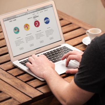A remote worker using a laptop to access a website with colorful icons on a wooden table with a coffee cup.